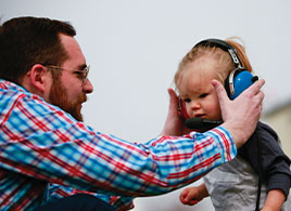 Photo of a man putting earmuffs on baby. Link to Life Stage Gift Planner Under Age 45 Situations.