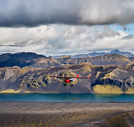 Photo of a plane flying over mountains. Link to What to Give.