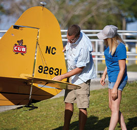 Photo of man and woman standing at tail of plane. Link to Gifts from Retirement Plans.